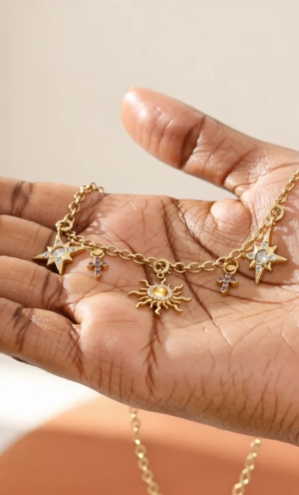 Bracelet à charms dorés — étoiles du Nord, soleil et croix — posé au creux d'une main
