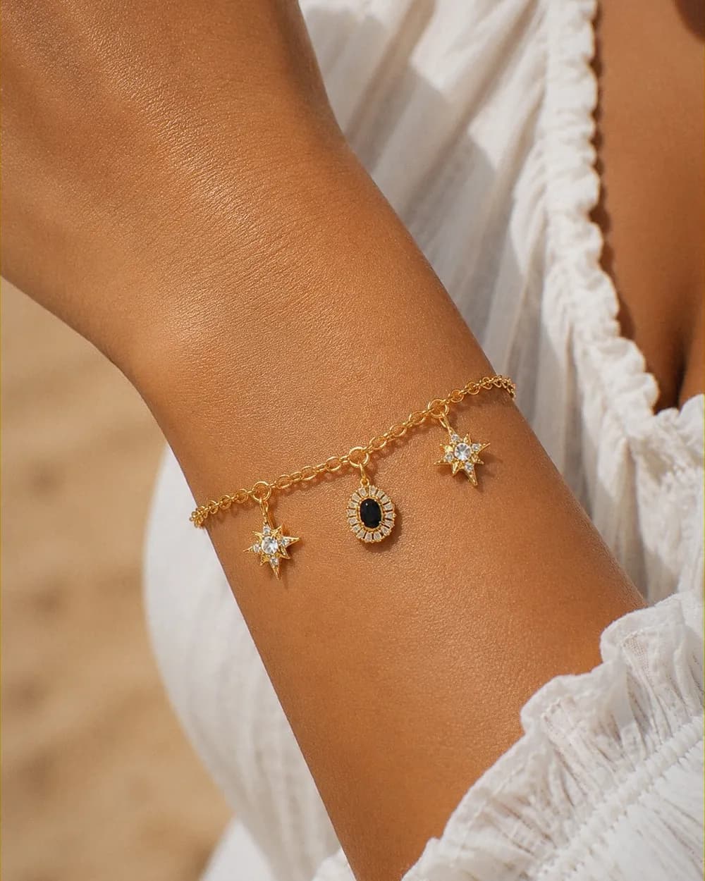 Bracelet à charms dorés — deux étoiles du Nord et un médaillon à pierre noire — porté au poignet