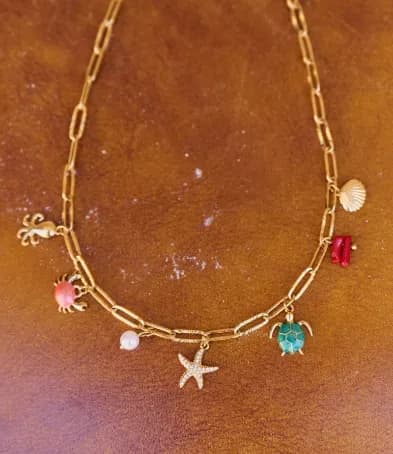 Collier à charms bord de mer posé sur un cuir fauve — crabe, étoile de mer, tortue, coquillage